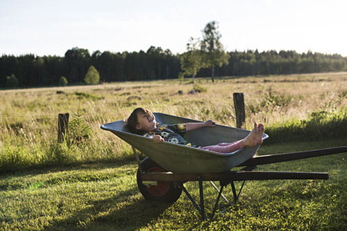 Jente i trillebår omgitt av grønne omgivelser