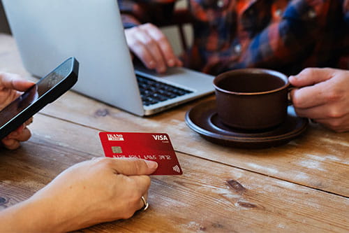 Dame sitter ved et bord og holder et Ikano Visa-kort