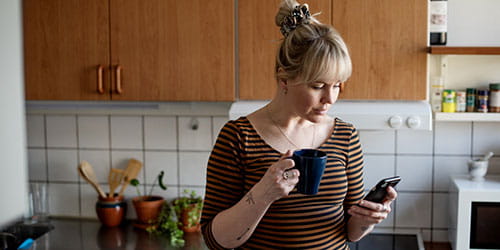 Kvinne på kjøkken søker om lån via mobilen