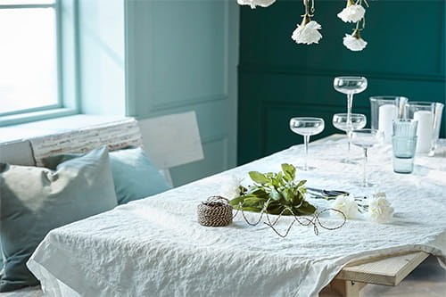 Trebenk med lyse pynteputer, bord med lys duk, glass og pynt.