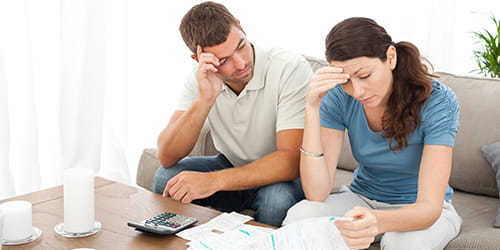 Bildet viser en kvinne og en mann som sitter sammen i en sofa og ser på papirer. Ved siden av dem står en kalkulator, og kvinnen har en penn i hånden. Antagelig diskuterer de et finansieringsspørsmål.